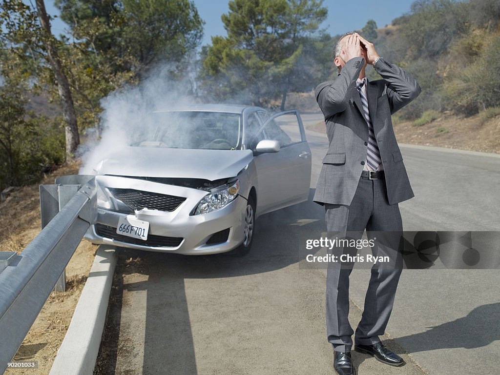 Frustrado hombre de negocios de pie al lado de coches wrecked en guardrail