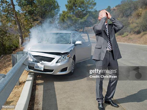 frustrated businessman standing next to car wrecked on guardrail - ongeluk transportatie evenement stockfoto's en -beelden