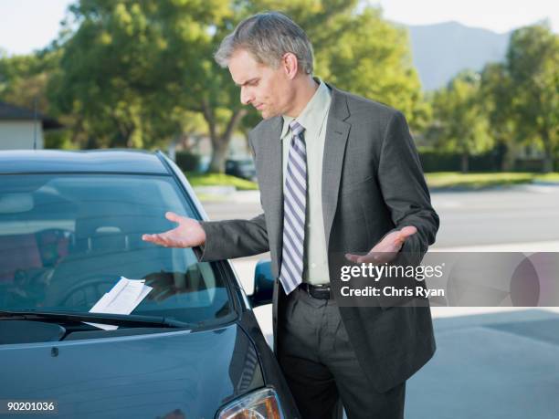 frustrated businessman viewing parking ticket on windshield - infrações de estacionamento - fotografias e filmes do acervo