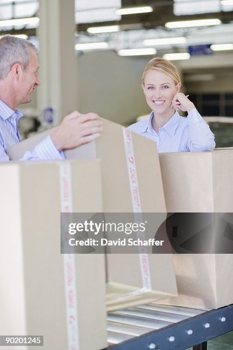 Co-workers standing with boxes on conveyor belt Co-workers standing with boxes on conveyor belt