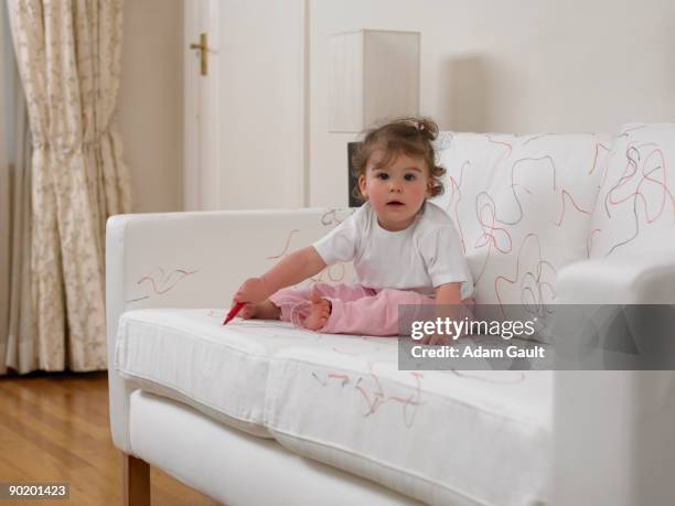 baby girl using marker on sofa - achtlos stock-fotos und bilder