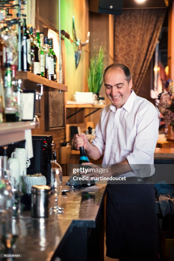 Camarero abriendo botella de vino detrás de una barra contraria.