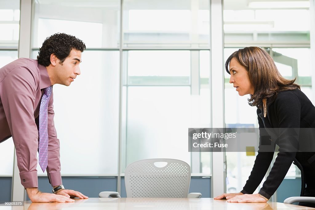 Two businesspeople facing off over conference room table