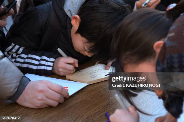 Young students write their wishes on Ema, wooden votive tablets with wishes on them, at Yushima Tenmangu Shrine in Tokyo on January 7, 2018. Many...