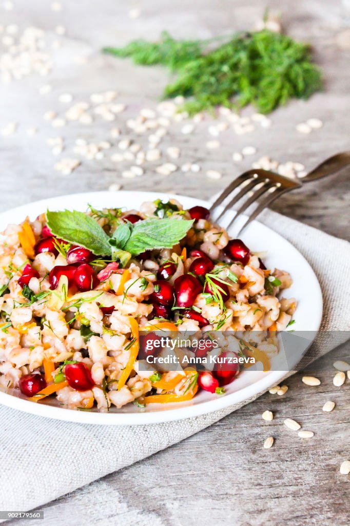 Warm salad with barley, carrot, onion, pomegranate seeds and fresh mint in a plate on a wooden table, selective focus