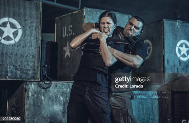 young woman using krav maga fighting self defense against male assailant in dark indoor urban setting - krav maga stock pictures, royalty-free photos & images