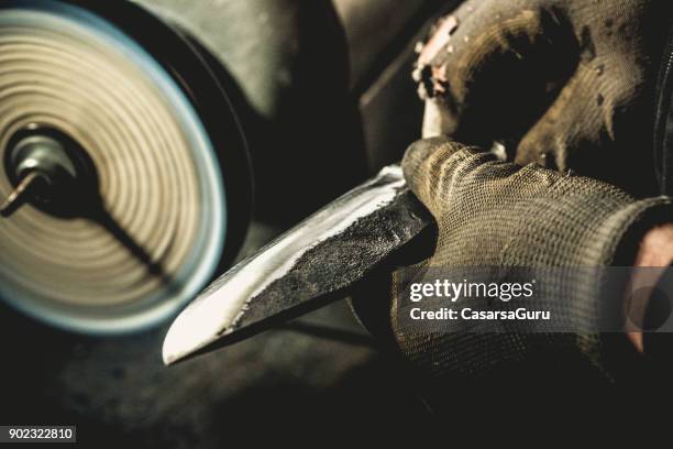 smid holding een mes bij een machine polijsten - smederij stockfoto's en -beelden