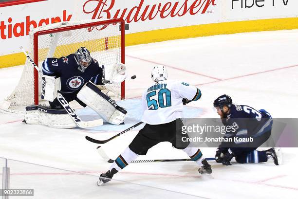 Goaltender Connor Hellebuyck of the Winnipeg Jets guards the net as Chris Tierney of the San Jose Sharks shoots the puck past a defending Toby...