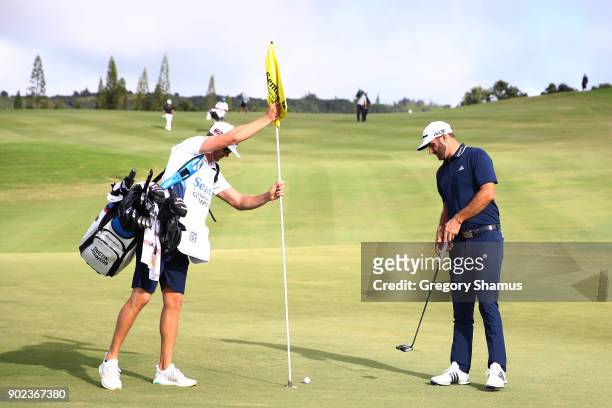 Caddie Austin Johnson pulls the pin flag as Dustin Johnson of the United States prepares to tap in for eagle on the 12th green during the final round...
