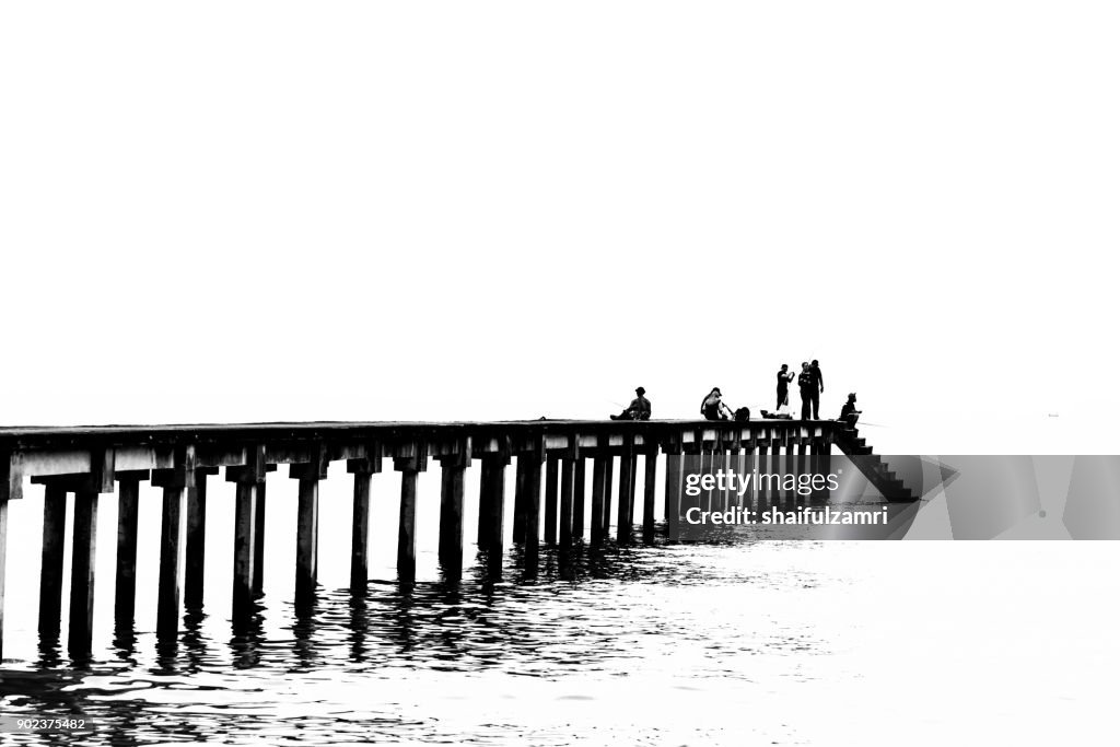 TELUK PELANDUK, MALAYSIA - 24TH DEC 2017; People cast the fishing rod to the sea. Black and white for classic view on old jetty. The old jetty still use for fisherman on fishing activities.