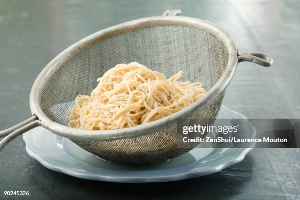 spaghetti in metal colander resting on plate - salatsieb stock-fotos und bilder
