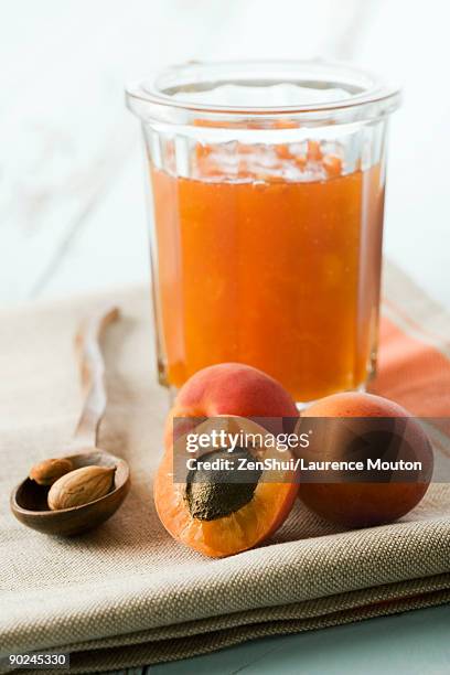 apricots, one cut open to reveal pit, jar of preserves in background - aprikosenkonfitüre stock-fotos und bilder