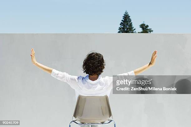 woman seated facing wall, arms outstretched, rear view - blouse back stock pictures, royalty-free photos & images