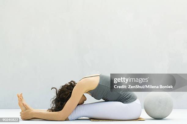 woman seated, bending forward to touch forehead to knees, fitness ball behind - tocar nos dedos dos pés imagens e fotografias de stock