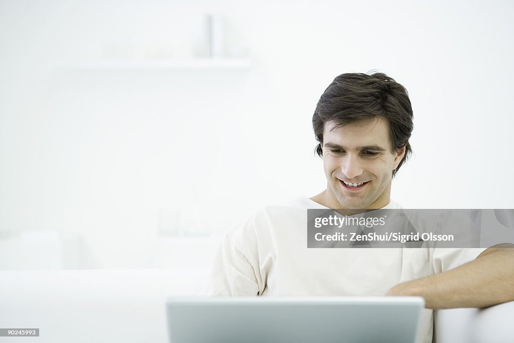 Man sitting on sofa, using laptop