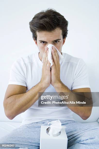 man blowing his nose with a tissue, looking at camera - tissue box stockfoto's en -beelden