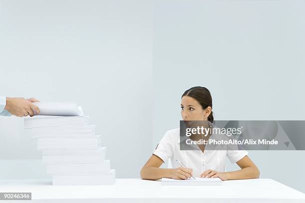 woman sitting at table, looking at a staggered stack of paper, man's hands adding paper to the pile - next to stock pictures, royalty-free photos & images