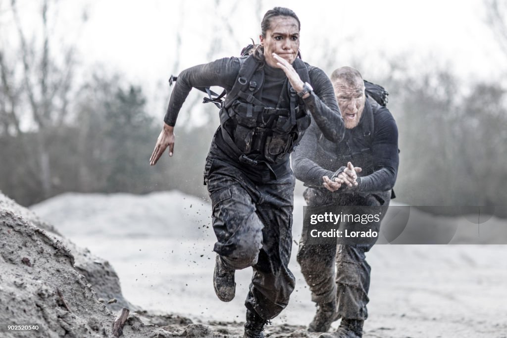 Redhead male drill instructor training beautiful brunette female soldier doing sprints outdoors in the mud