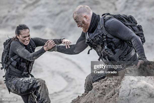 redhead male and brunette female military members training hard and helping each other on a sand hill run - treino militar imagens e fotografias de stock