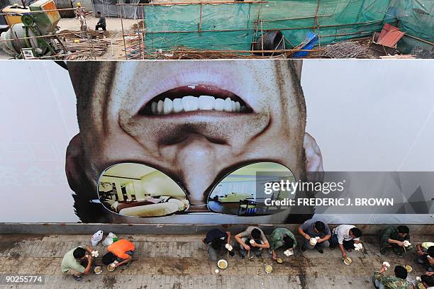 Construction workers eat their lunch in front of a billboard surrounding the site for new urban housing which they are helping to build in Beijing on...