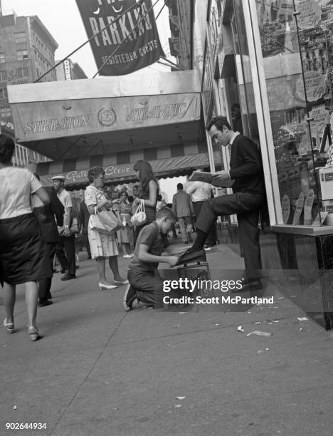 Young boy shines a man's shoes as he reads the papers on Seventh avenue in front of the Sheraton hotel in Times Square, New York.