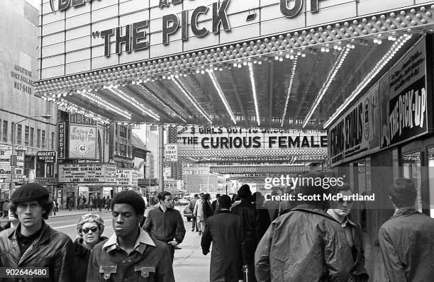 Pedestrians walk under the many adult movie theater marquees showing pornography films that line 42nd street in the heart of Times Square, New York.