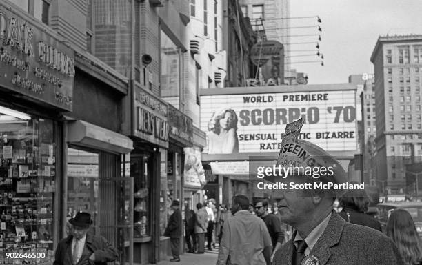 Man working for a sight seeing company, stands near the marquee of an adult movie theater showing pornography films on 42nd street in Times Square,...