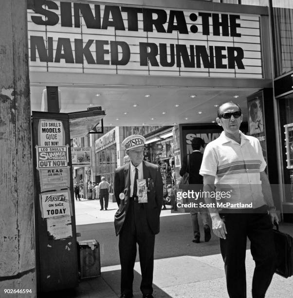 Sight seeing tour operator waits for customers, as pedestrians walk under a movie theater marquee showing the Frank Sinatra film The Naked Runner on...