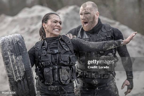 roodharige mannelijke drill-instructeur opleiding van mooie brunette vrouwelijke soldaat met behulp van banden buiten in de modder - sergeant instructeur stockfoto's en -beelden