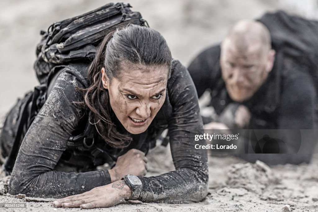 Redhead male and brunette female military swat security anti terror duo crawling  together during operations in muddy sand