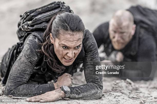 redhead male and brunette female military swat security anti terror duo crawling together during operations in muddy sand - special forces stock pictures, royalty-free photos & images