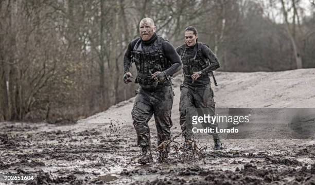 redhead male and brunette female military swat security anti terror duo during operations in outdoor muddy setting - army officer stock pictures, royalty-free photos & images