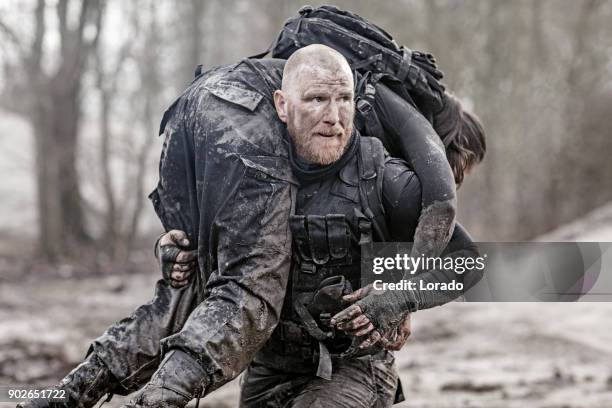 macho shaven headed redhead male military swat security anti terror member carrying female team member during operations - police rescue stock pictures, royalty-free photos & images