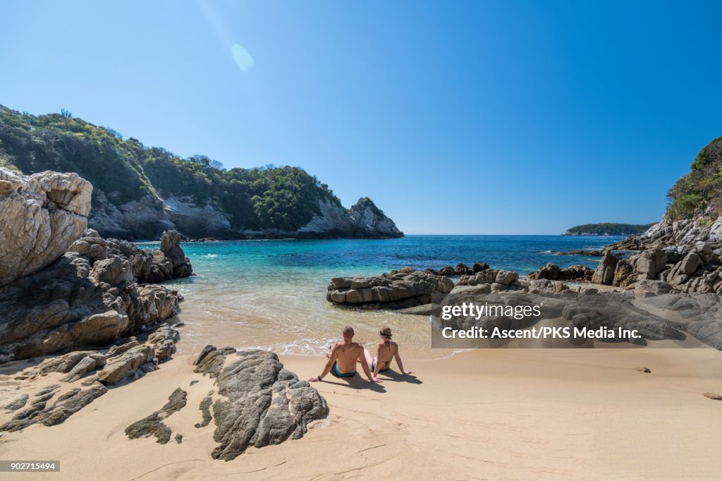 Couple relax on beach, look out to sea