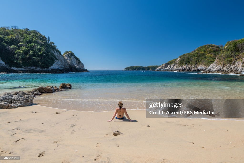 Woman relaxes on beach, looks out to sea