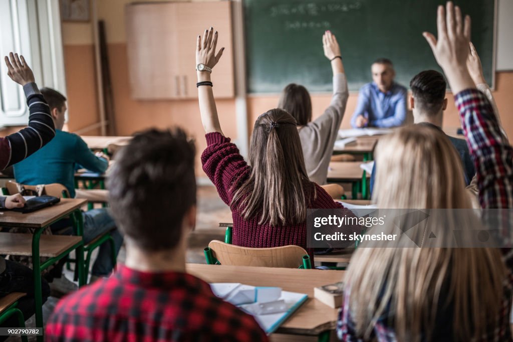 Rear view of high school students with raised arms during the class.