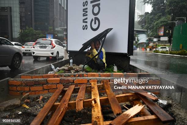 Worker takes shelter from the rain in Kuala Lumpur on January 9, 2018.