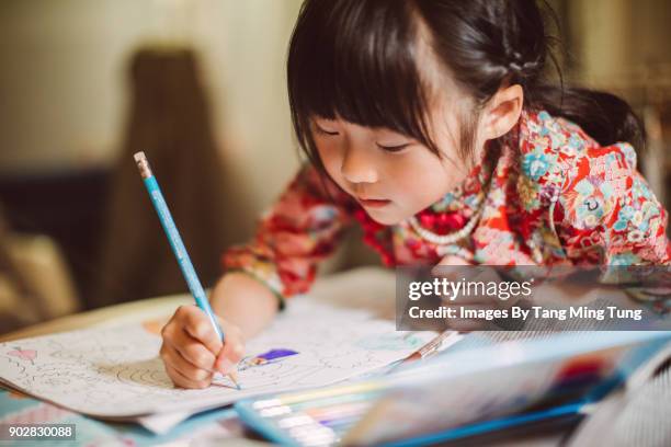 lovely little girl in traditional chinese costumes colouring in a colouring book happily. - chinese person stockfoto's en -beelden