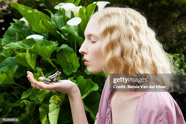 young woman preparing to kiss frog. - woman frog hand stock-fotos und bilder