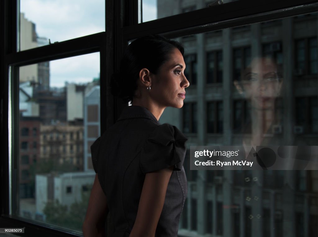Woman looking over city, reflected in window