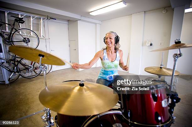 mature woman bangs drums in garage - drums stock-fotos und bilder