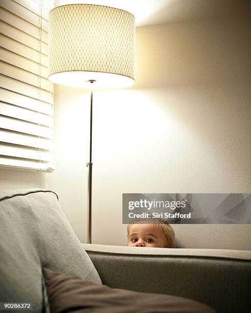 young boy hiding behind couch, peeking over armres - lampenschirm stock-fotos und bilder