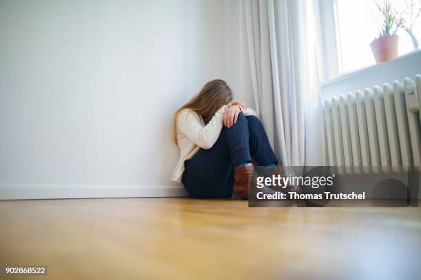 Posed scene on the topic of depression: A young woman is sitting in the corner of a room with her head resting on her arms on January 08, 2018 in...