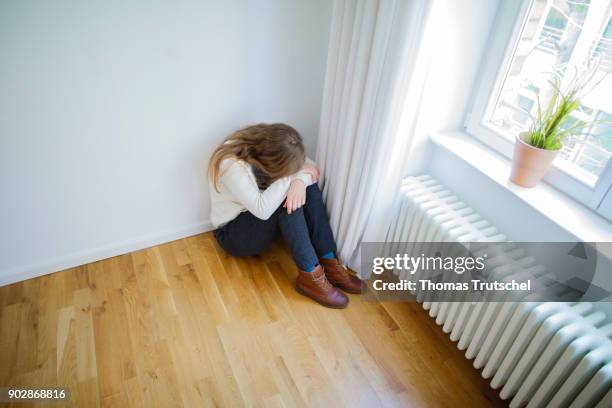 Berlin, Germany Posed scene on the topic of depression: A young woman is sitting in the corner of a room with her head resting on her arms on January...