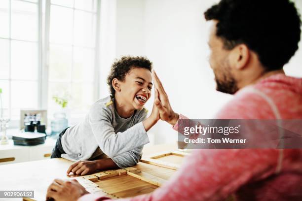 young boy high fives dad during game of dominoes - family game stock-fotos und bilder