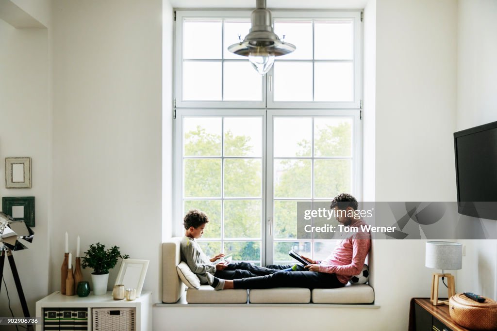 Father And Son Relaxing By Large Window At Home