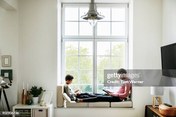 father and son relaxing by large window at home - family ipad stockfoto's en -beelden