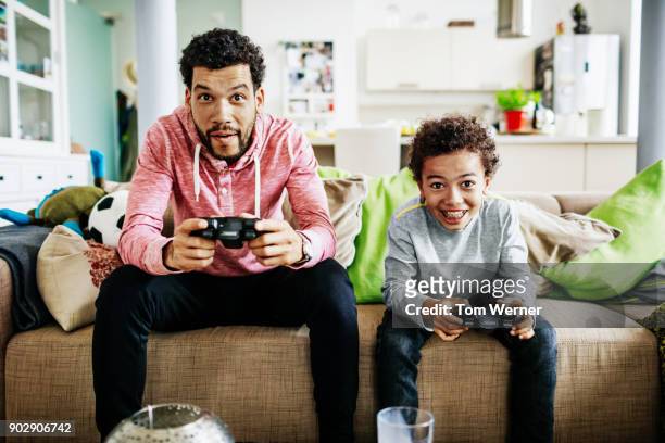 father and son concentrating while playing video games together - giocare foto e immagini stock