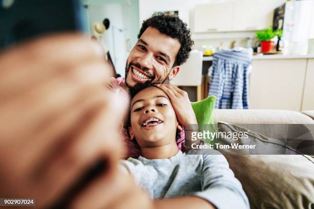 father and son taking selfie together at home using smartphone - western europe stock pictures, royalty-free photos & images
