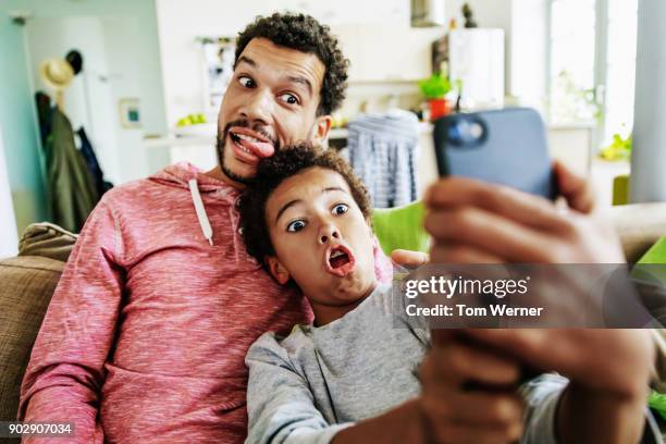 father and son pulling silly faces while taking selfie together - quirky family stockfoto's en -beelden